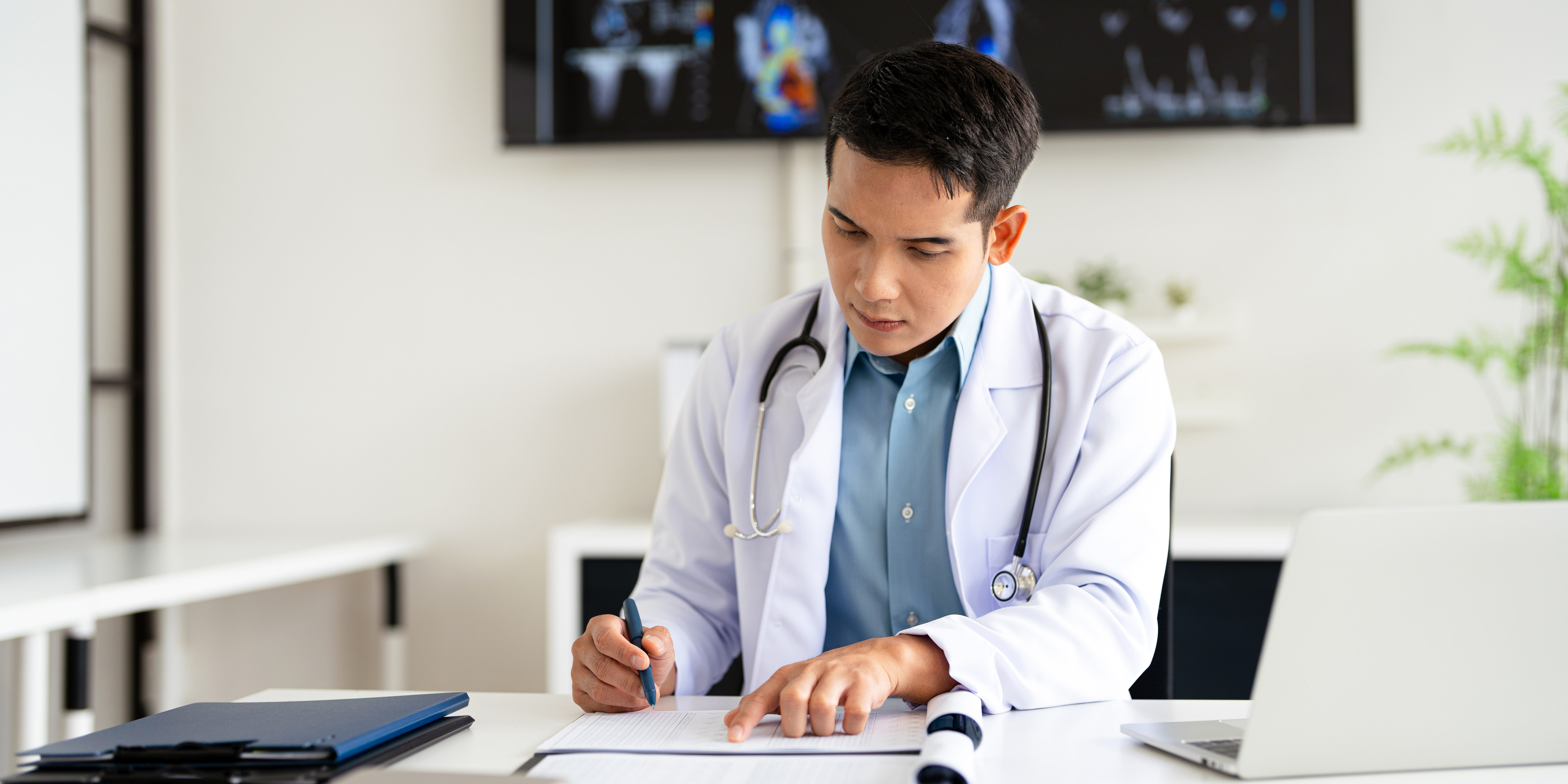 Physician completing a medical form beside diagnostic scan monitors