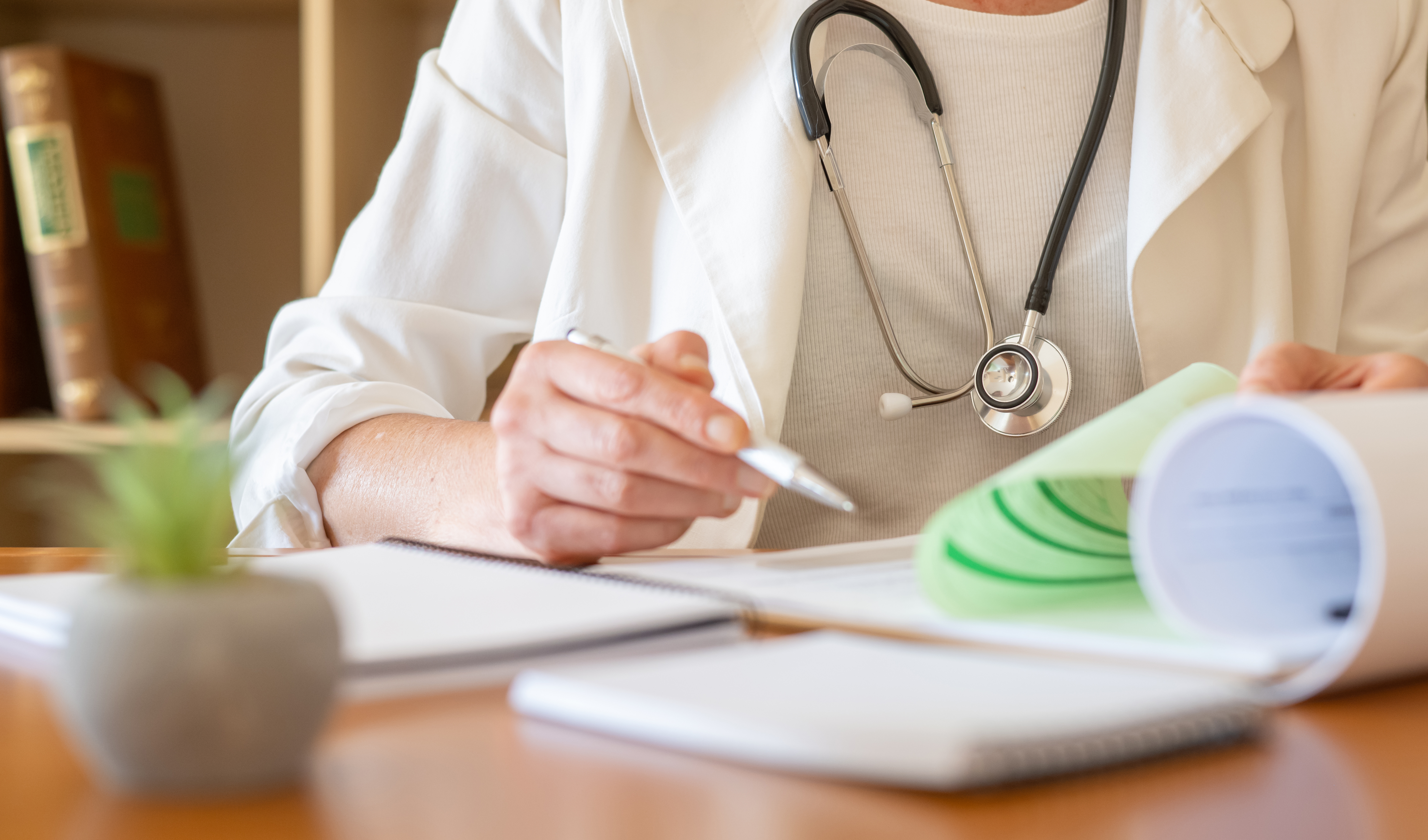 Doctor taking notes beside medical reference materials during impairment evaluation