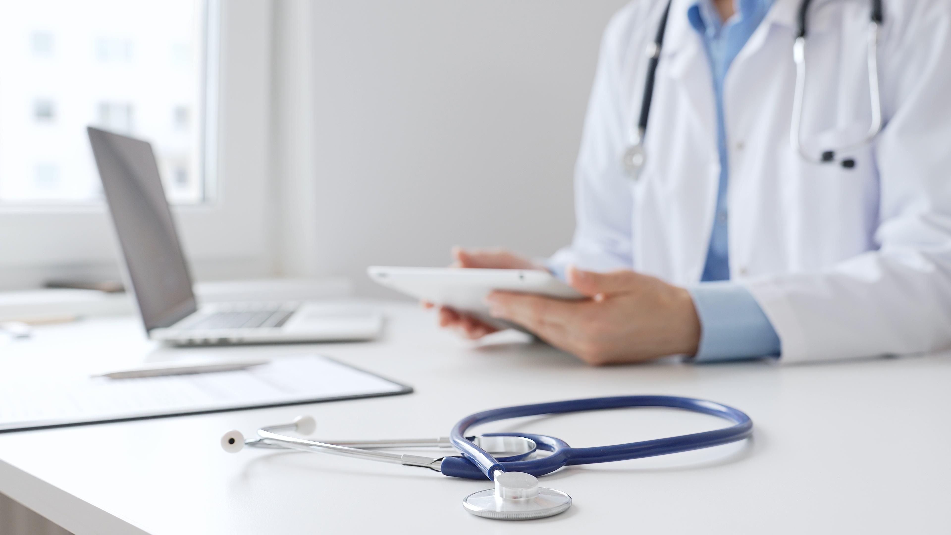 Doctor using tablet to review clinical data with medical equipment on desk