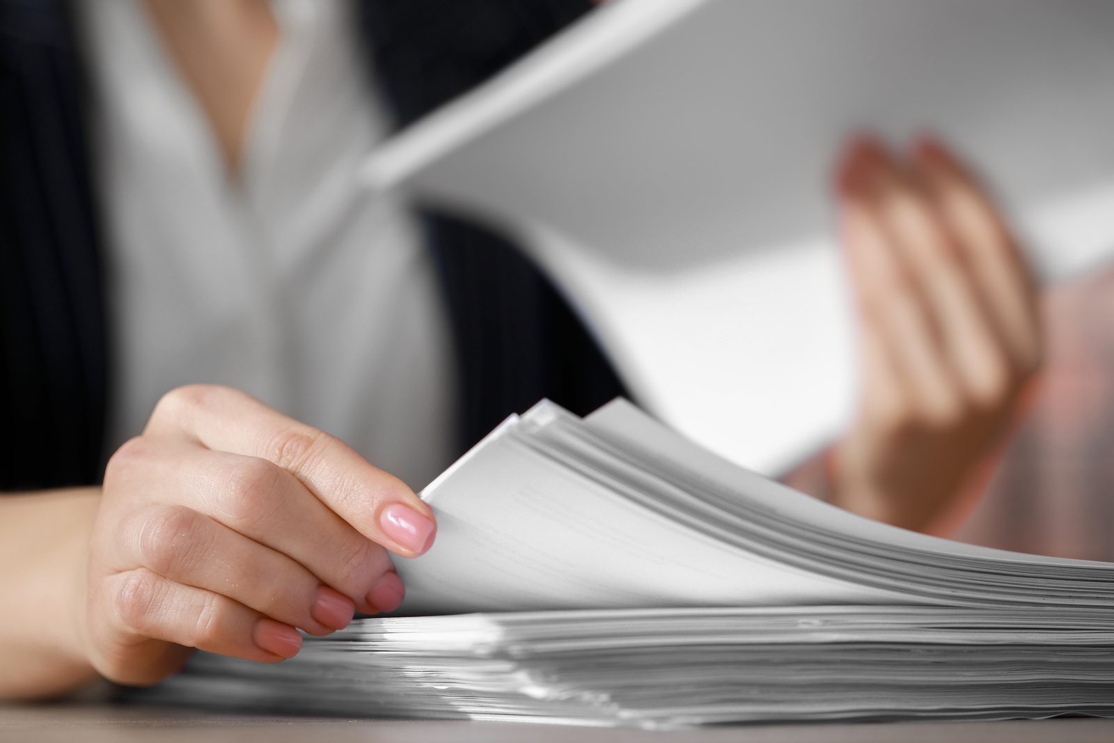 A reviewer flipping through a thick stack of paper medical records